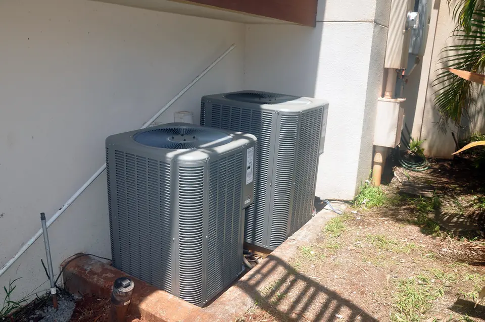 Two outdoor air conditioning condensers on a concrete pad beside a house