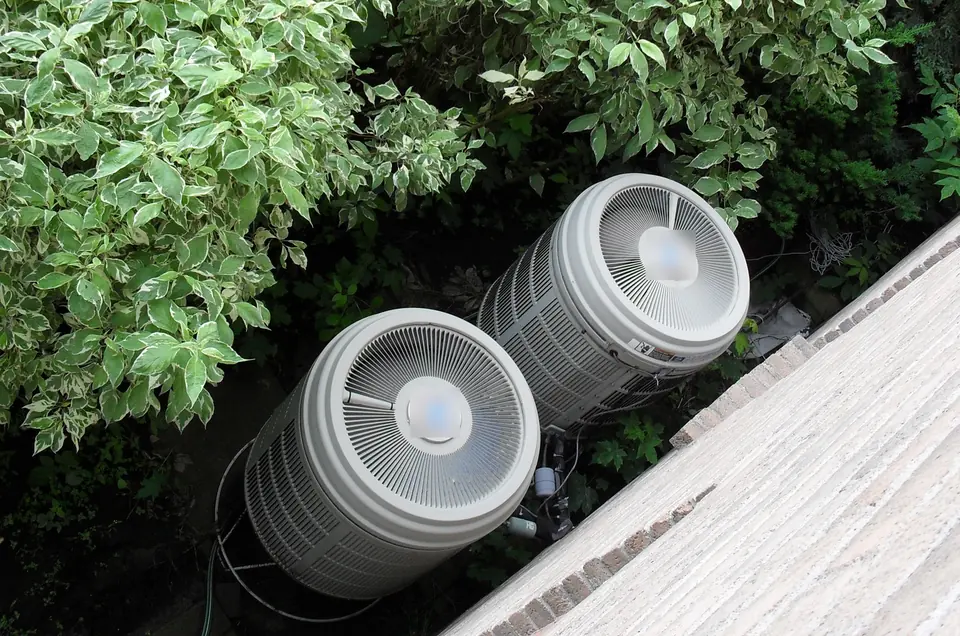 Two round outdoor heat pump units surrounded by green shrubs